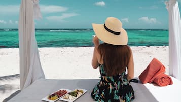 Una persona sentada en una mesa con vista al mar, un plato de comida y una toalla enrollada.