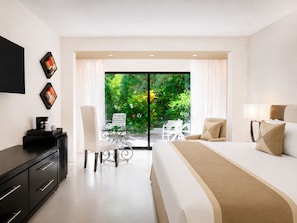 A hotel room with a bed, a desk, a chair, and a balcony with a view of greenery.