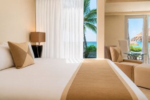 Habitación de hotel con cama, zona de estar con mesa y vista al océano.
