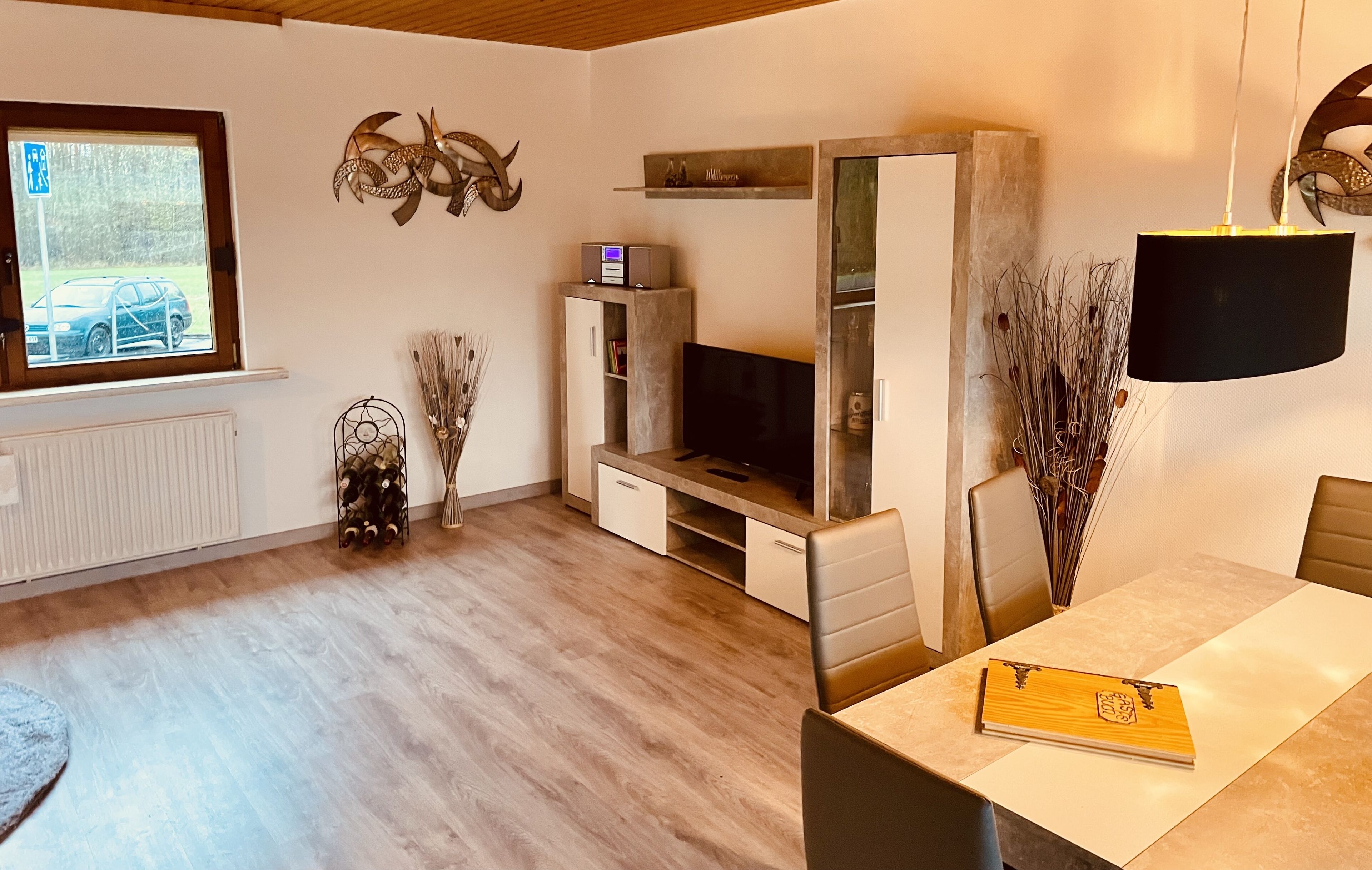 A modern living room with a TV, wooden cabinet, and a dining area with a table and chairs.