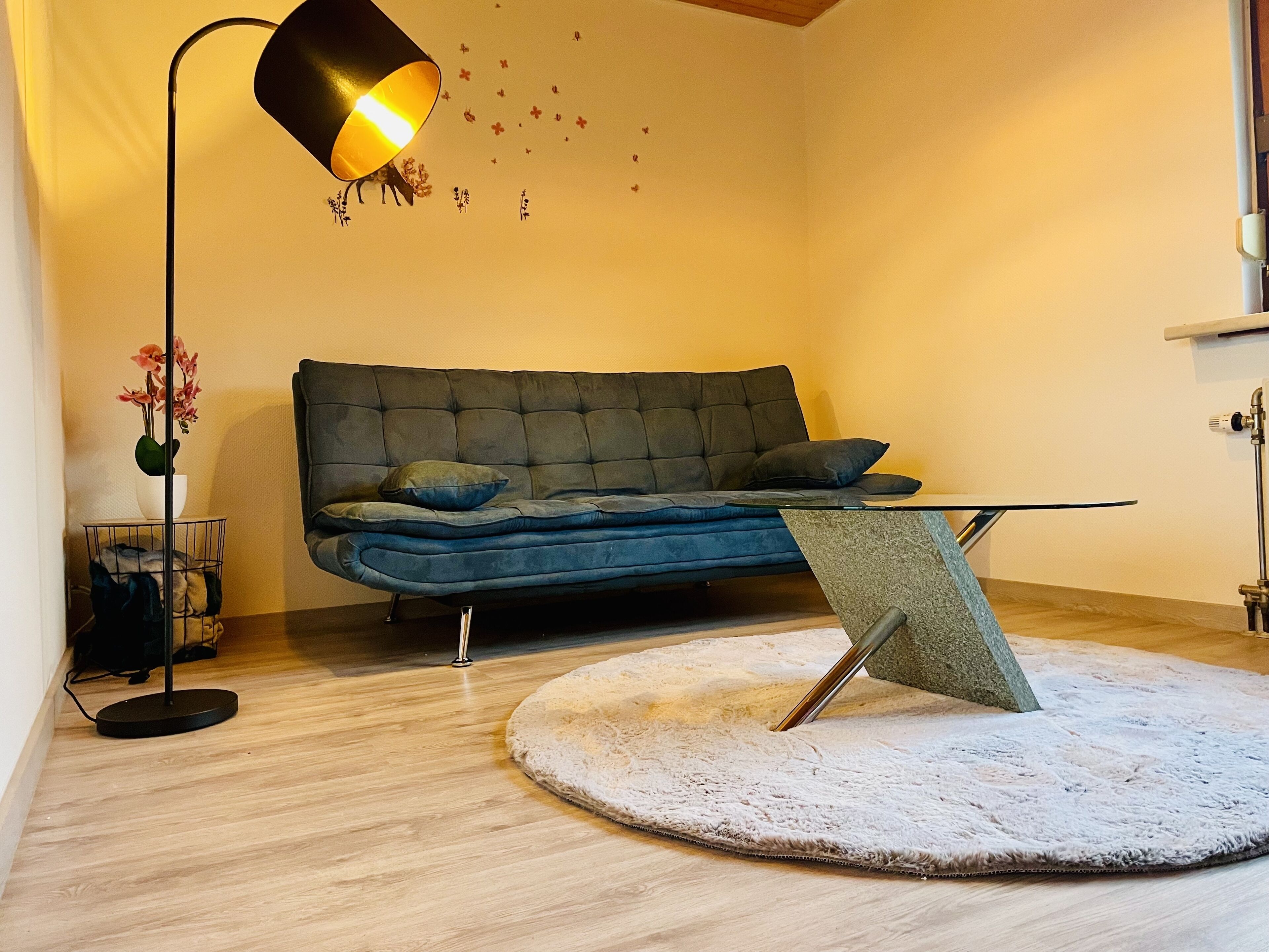 Un salon moderne avec un canapé bleu foncé, un tapis rond blanc, une lampe sur pied et une petite table.