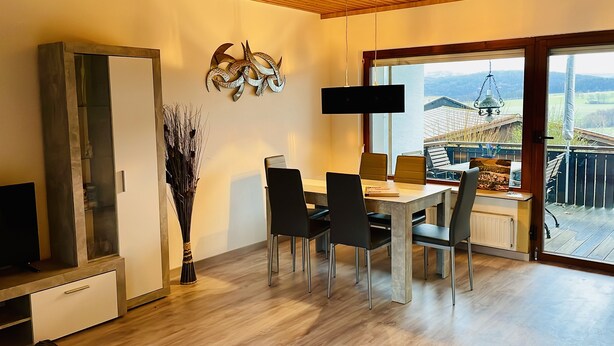A modern dining area with a wooden table, black chairs, and a decorative wall piece. - Gemütlicher Bungalow in Ruhiger Lage mit Traumhafter Aussicht für 2-6 Personen (Dipperz)