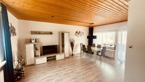 A spacious living area with a wooden ceiling, a dining table with chairs, a TV, and a cabinet. - Gemütlicher Bungalow in Ruhiger Lage mit Traumhafter Aussicht für 2-6 Personen (Dipperz)