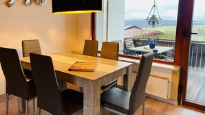 A dining area with a wooden table and chairs, a pendant light, and a view of a balcony with outdoor furniture. - Gemütlicher Bungalow in Ruhiger Lage mit Traumhafter Aussicht für 2-6 Personen (Dipperz)