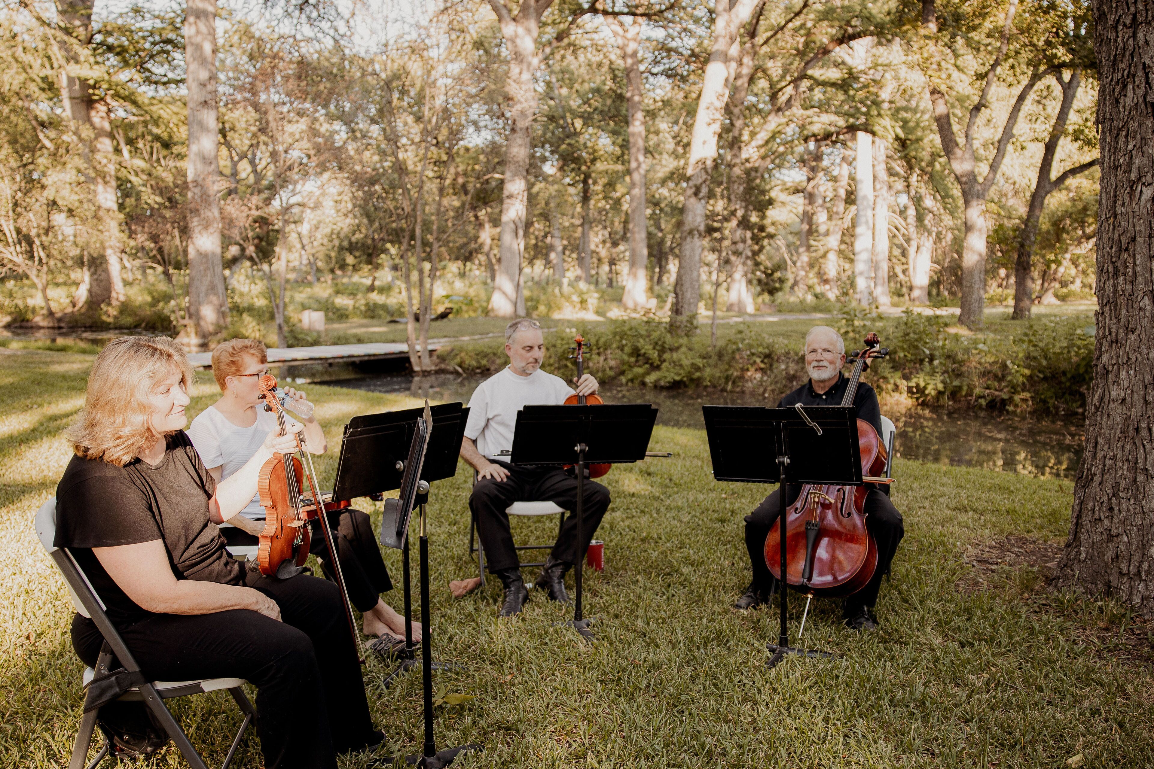A group of musicians seated outdoors with sheet music stands in front of them.