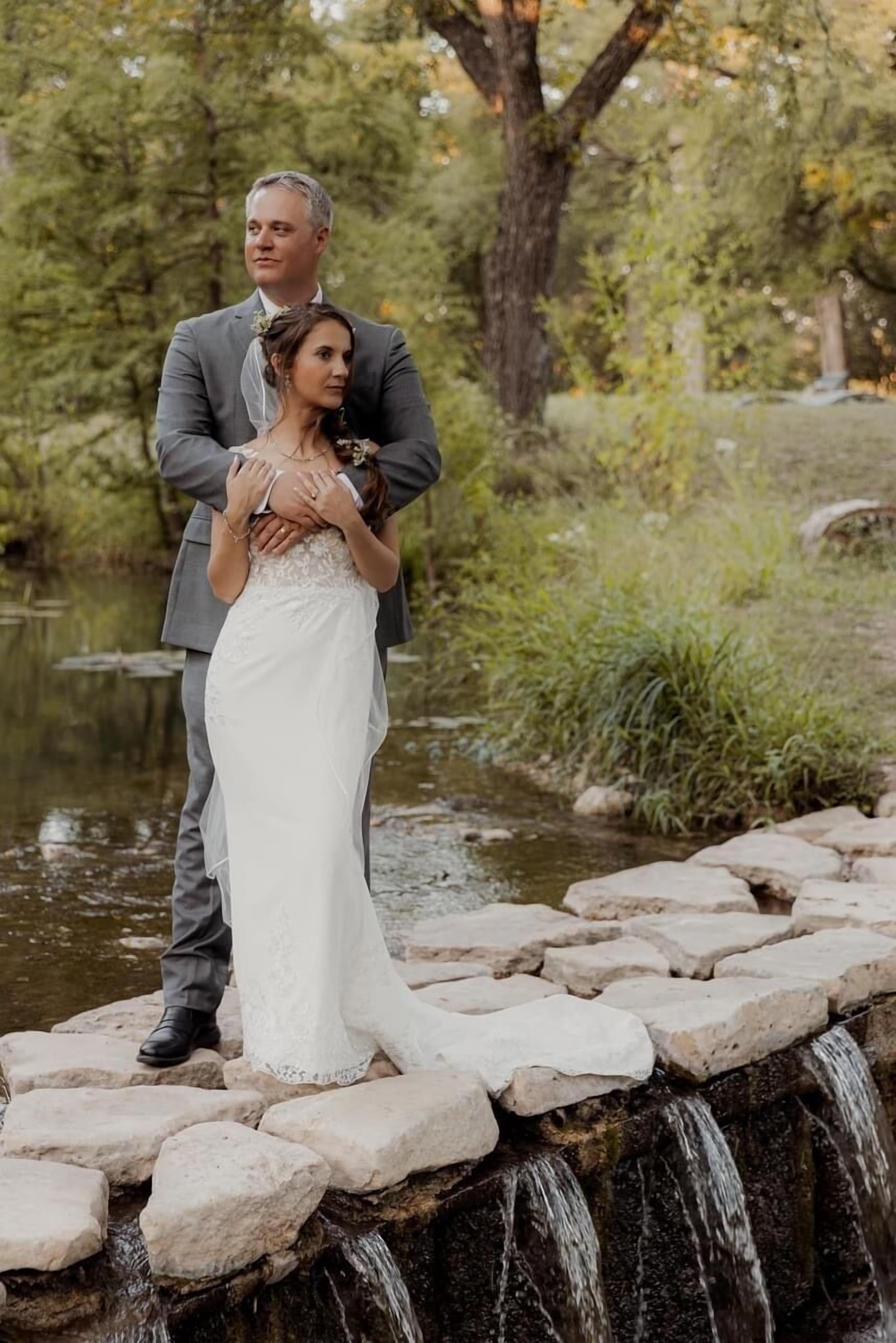 Un couple se tient sur un pont de pierre surplombant une petite cascade dans un parc.