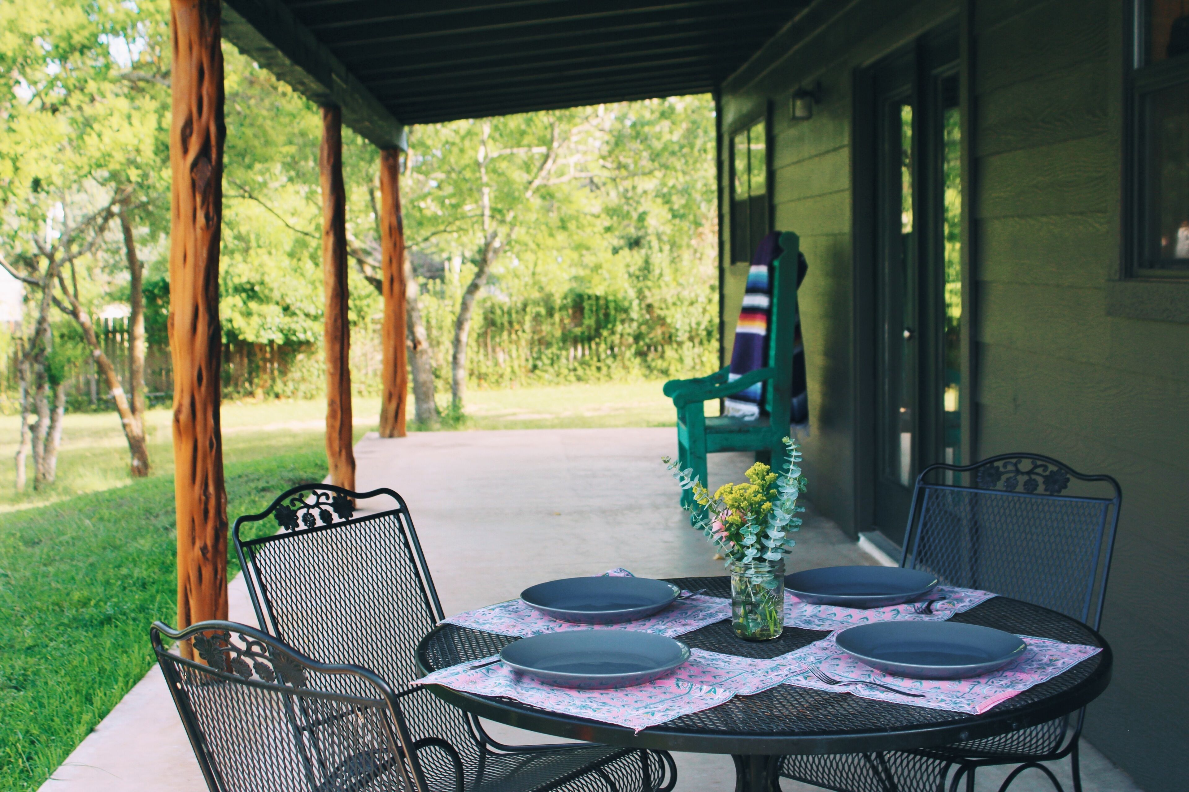 A covered patio with a table set for four, chairs, and a green chair in the background.