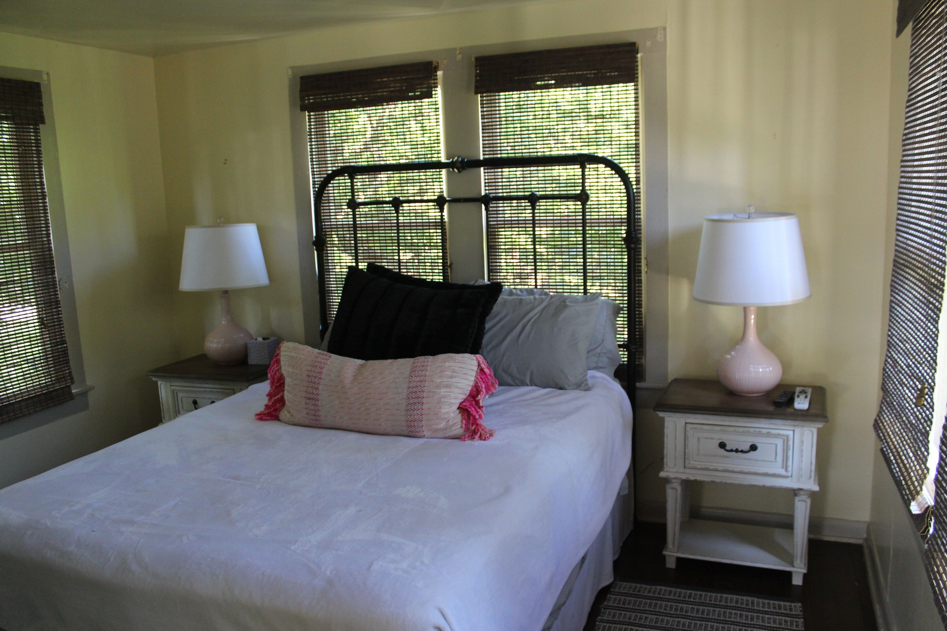 A bedroom with a bed, two bedside tables with lamps, and a window with blinds.