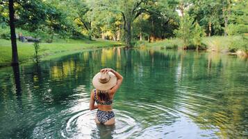 A woman in a swimsuit and hat standing in a calm body of water surrounded by greenery.