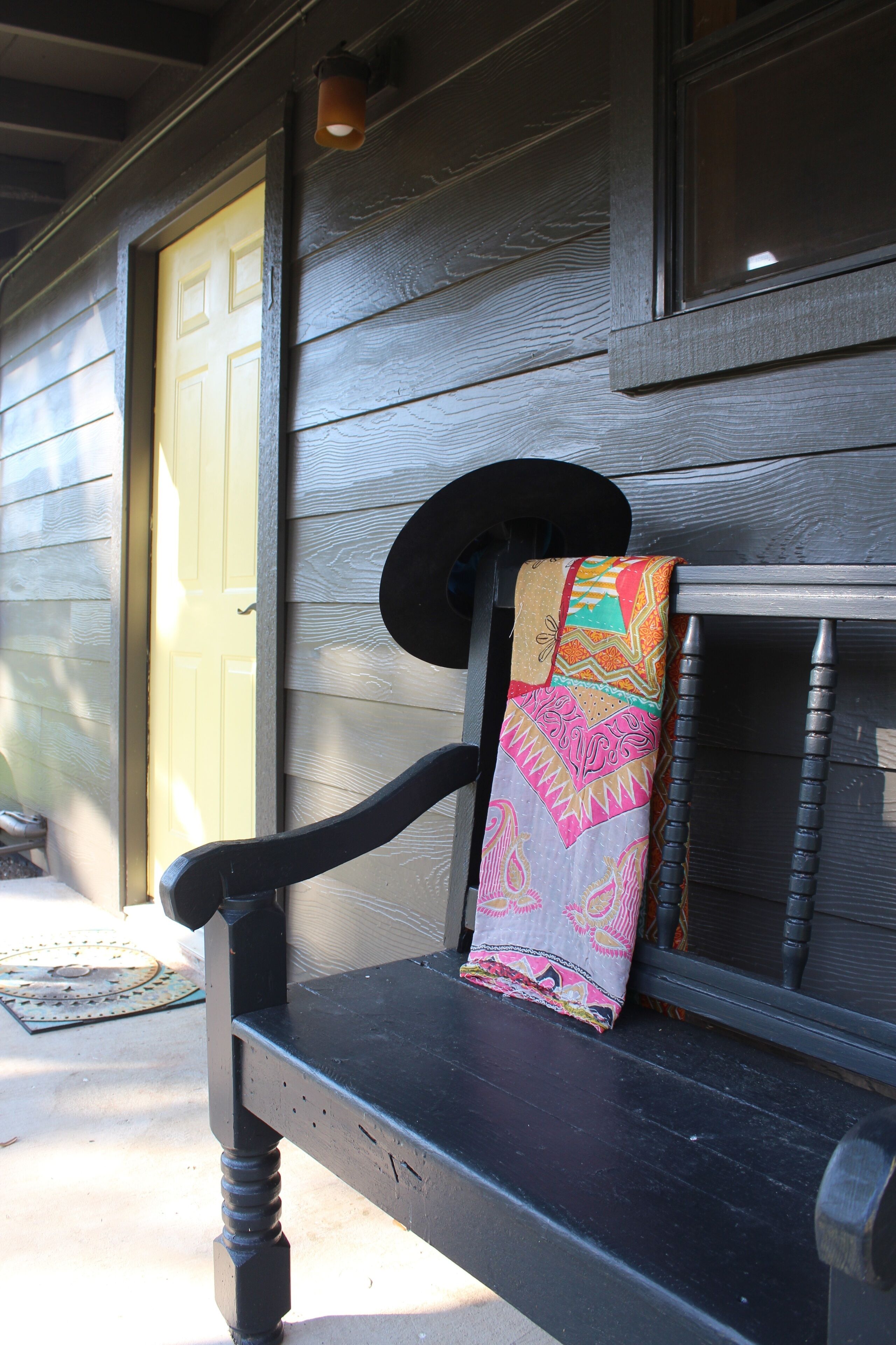 A wooden bench with a colorful fabric draped over it, positioned outside a building with a yellow door.