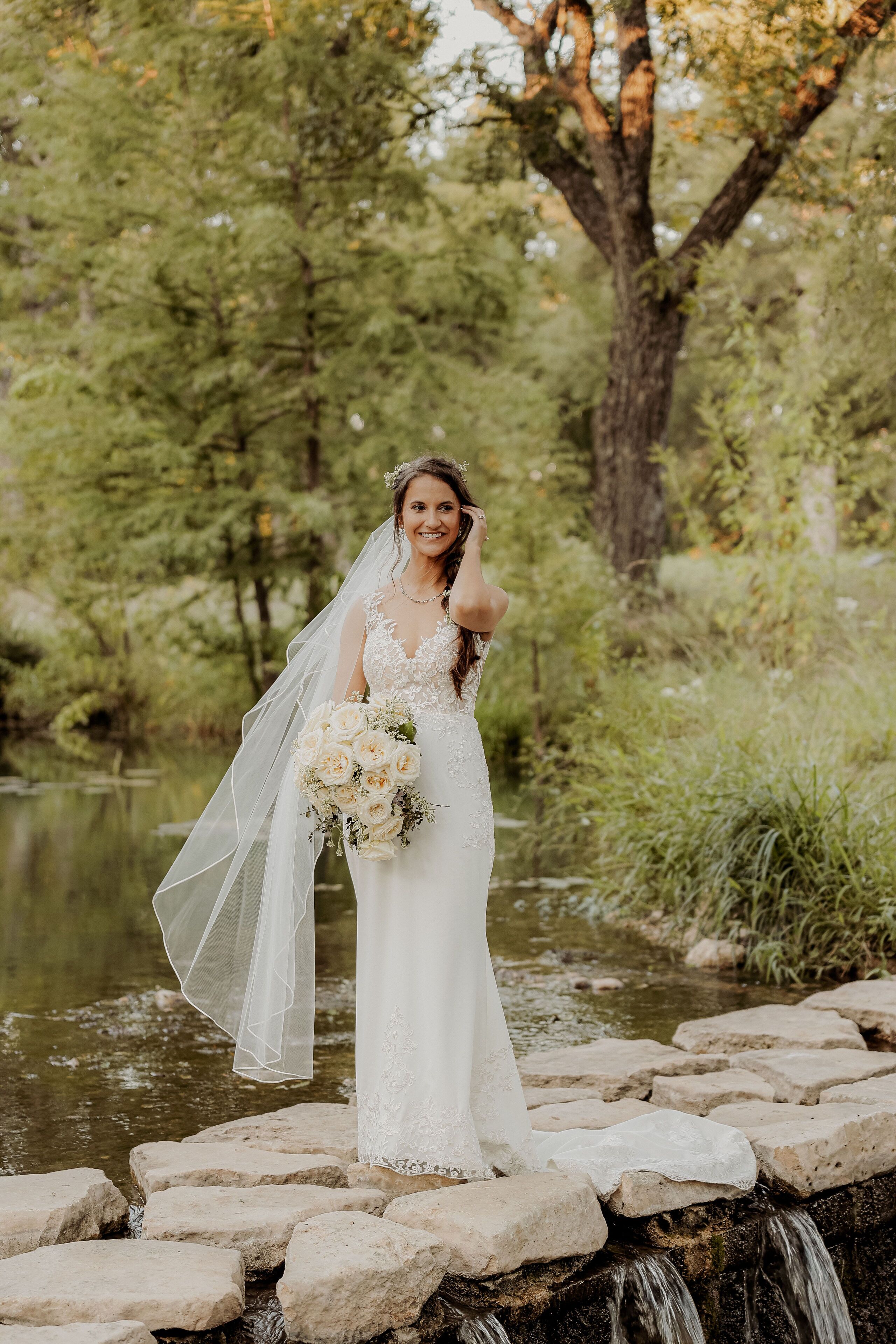 A bride standing on a stone bridge over a pond, holding a bouquet.