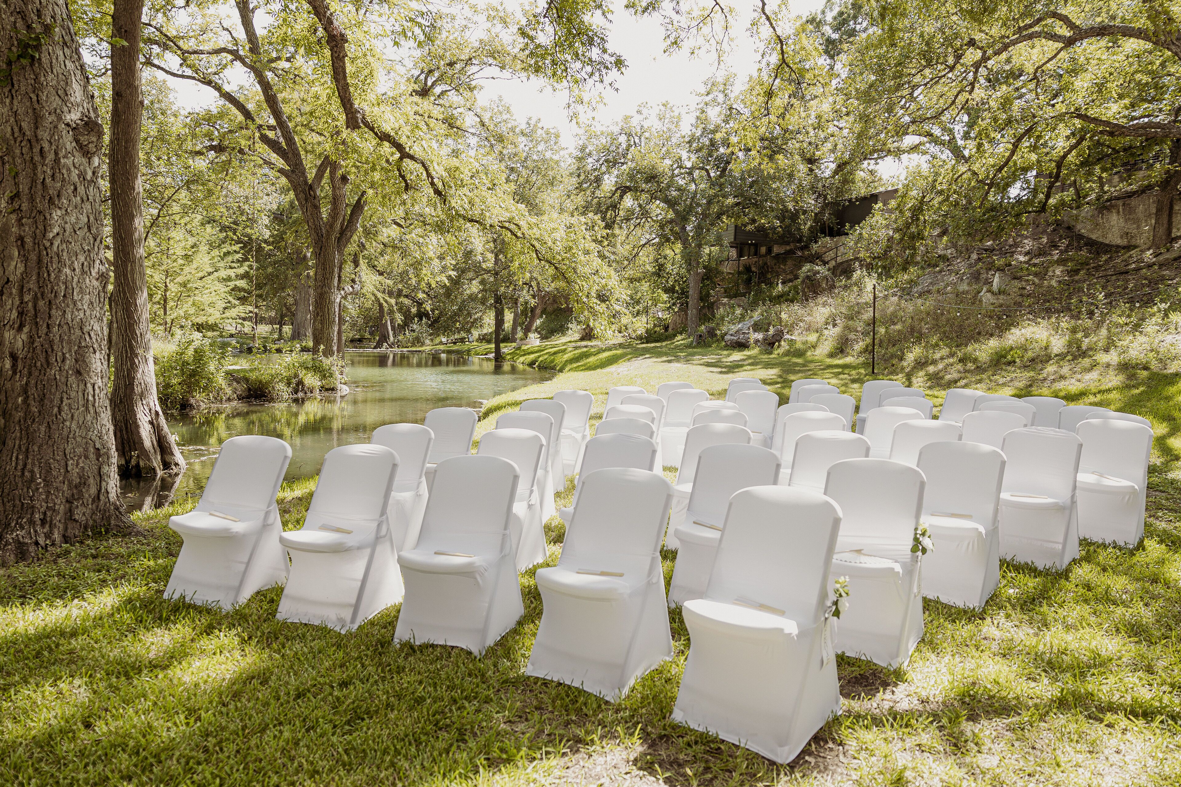 Een rij witte stoelen buiten, met op de achtergrond bomen en een wateroppervlak.