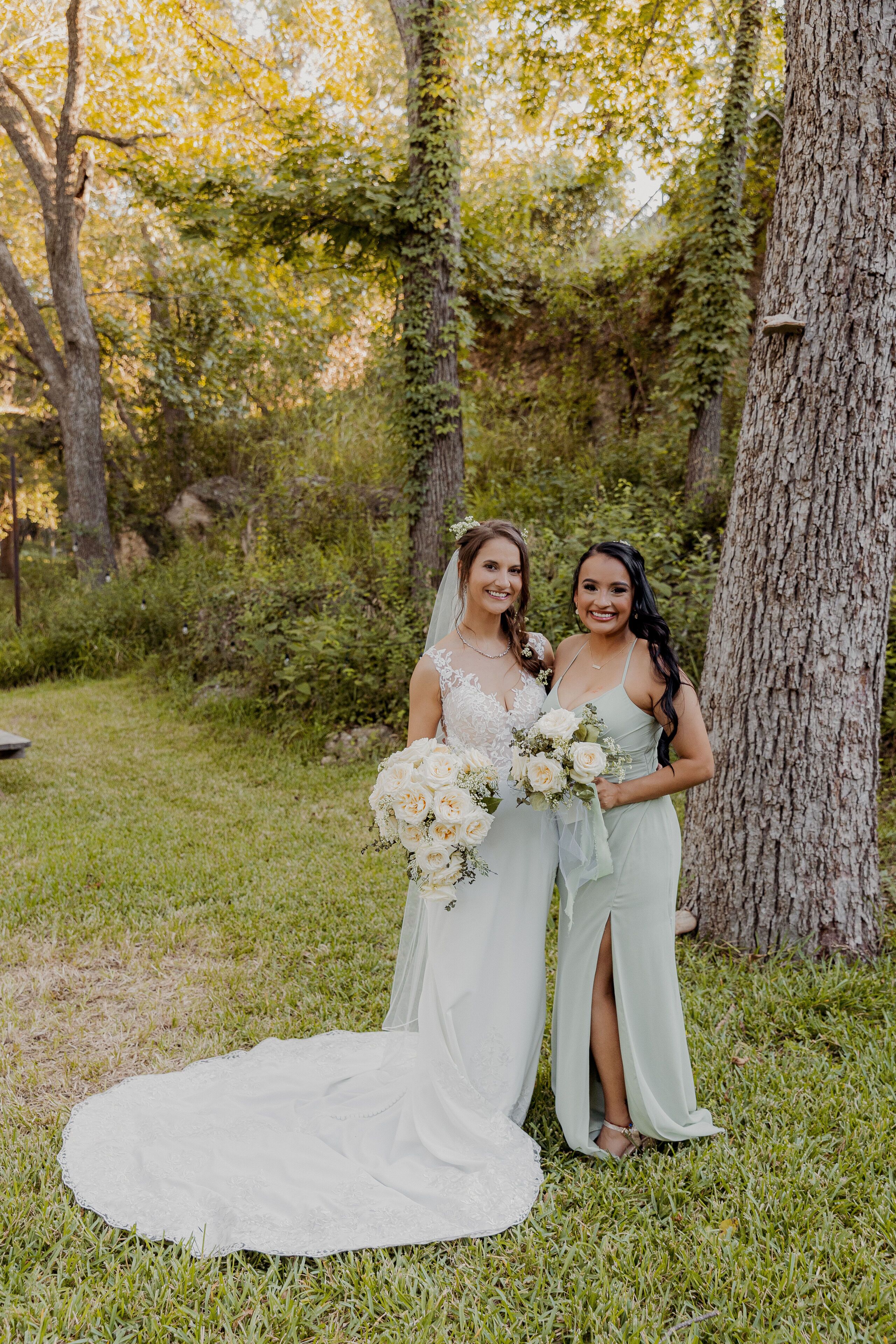 A wedding scene with a bride and two bridesmaids in a grassy outdoor area with trees.