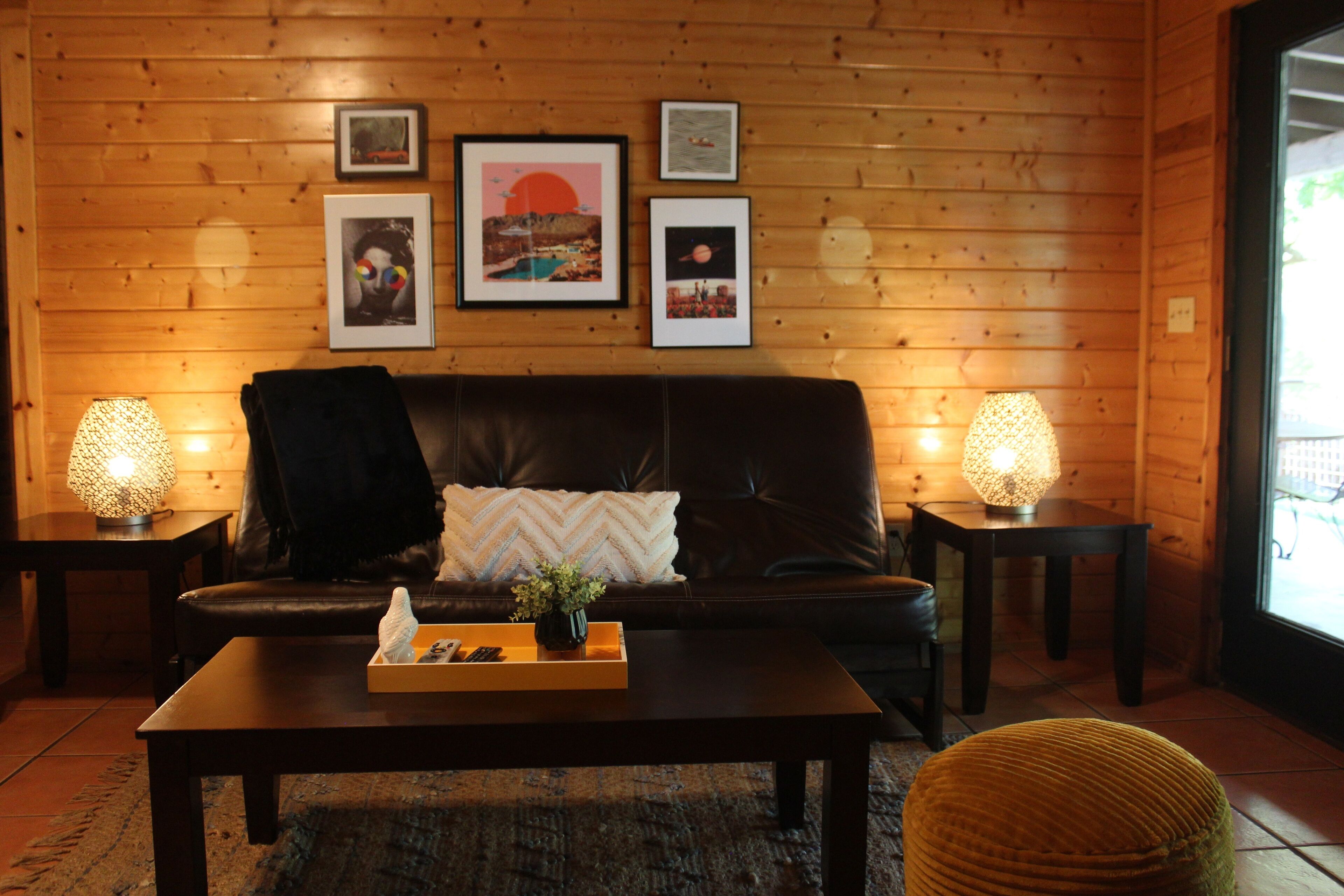 Een gezellige kamer met een leren bank, twee bijzettafels met lampen, een salontafel met dienblad en ingelijste foto's aan de muur.