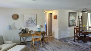 A room with a wooden floor, a dining table with chairs, a sofa, a small wooden stool, and a lamp. - Casa Las Palmeras (Port Richey)