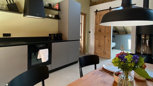 A kitchen with wooden beams, a black range hood, and a dining table with chairs.