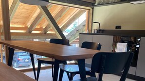 A dining area with wooden tables and black chairs, a kitchen in the background, and a view of a parked car outside.