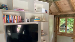 A modern living room with a large flat-screen TV, wooden bookshelves, and a window with a view of greenery.