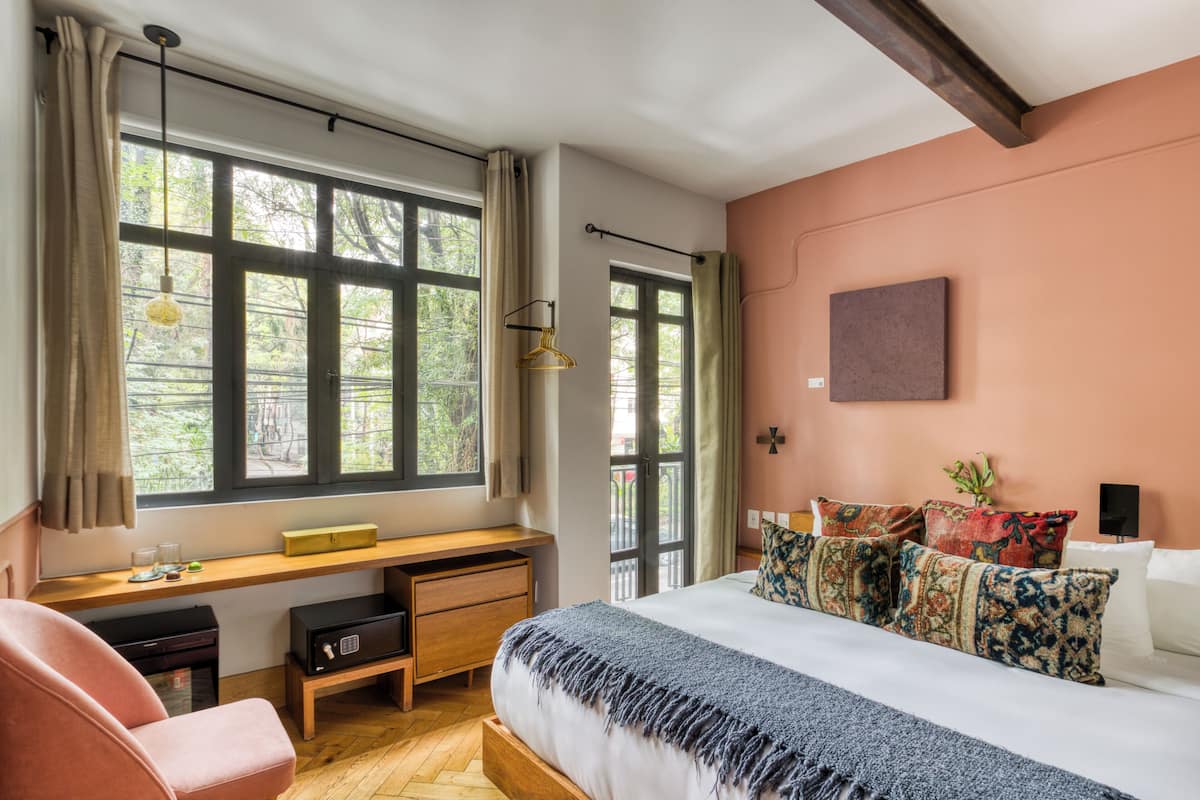 Un dormitorio con cama, escritorio, silla y ventanas amplias.