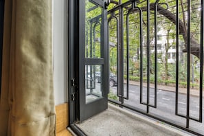 A door with a metal gate leading to a street with cars and greenery.