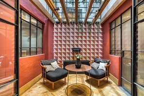 A room with two black cushioned chairs, a round wooden table, and a red and white geometric wall pattern.