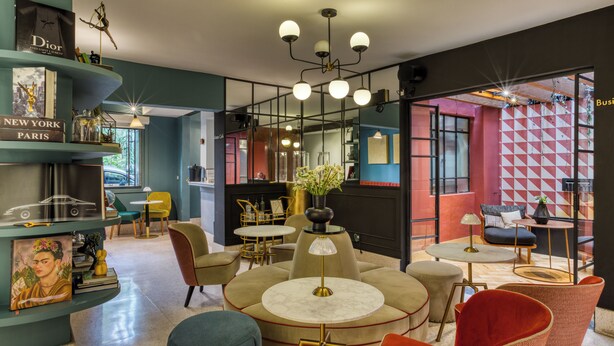 Un interior moderno con mesas redondas, sillas y una estantería con libros y objetos decorativos.