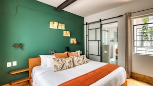 Un dormitorio con cama, paredes verdes, una ventana y una puerta corredera que da a un baño.