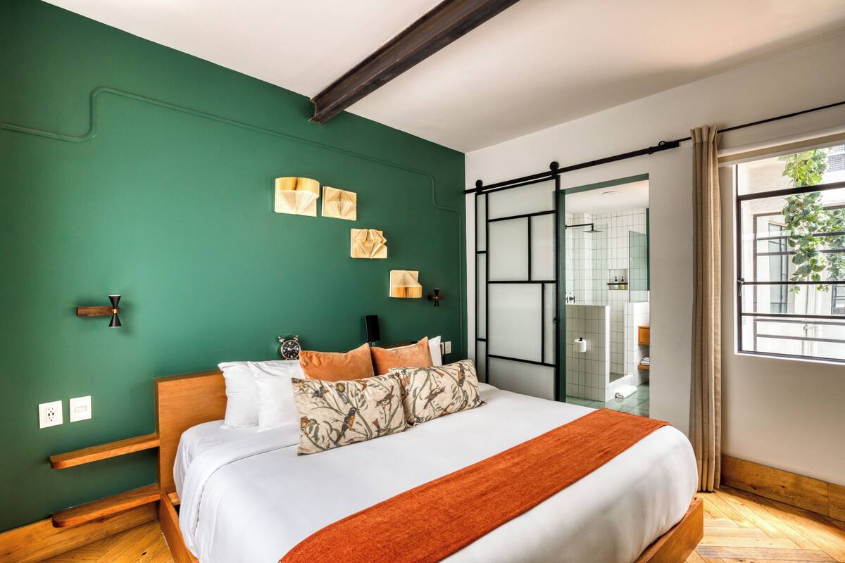 Un dormitorio con cama, paredes verdes, una ventana y una puerta corredera que da a un baño.
