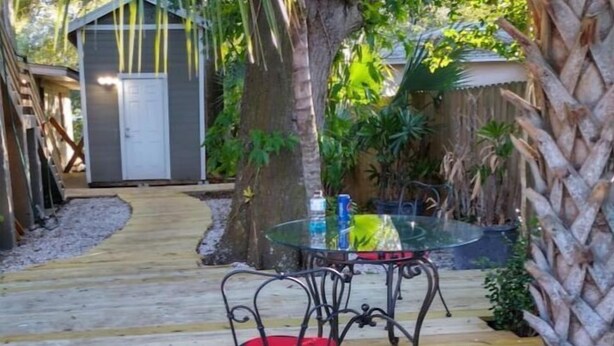Une terrasse en bois avec une table et des chaises en verre, entourée de plantes tropicales.