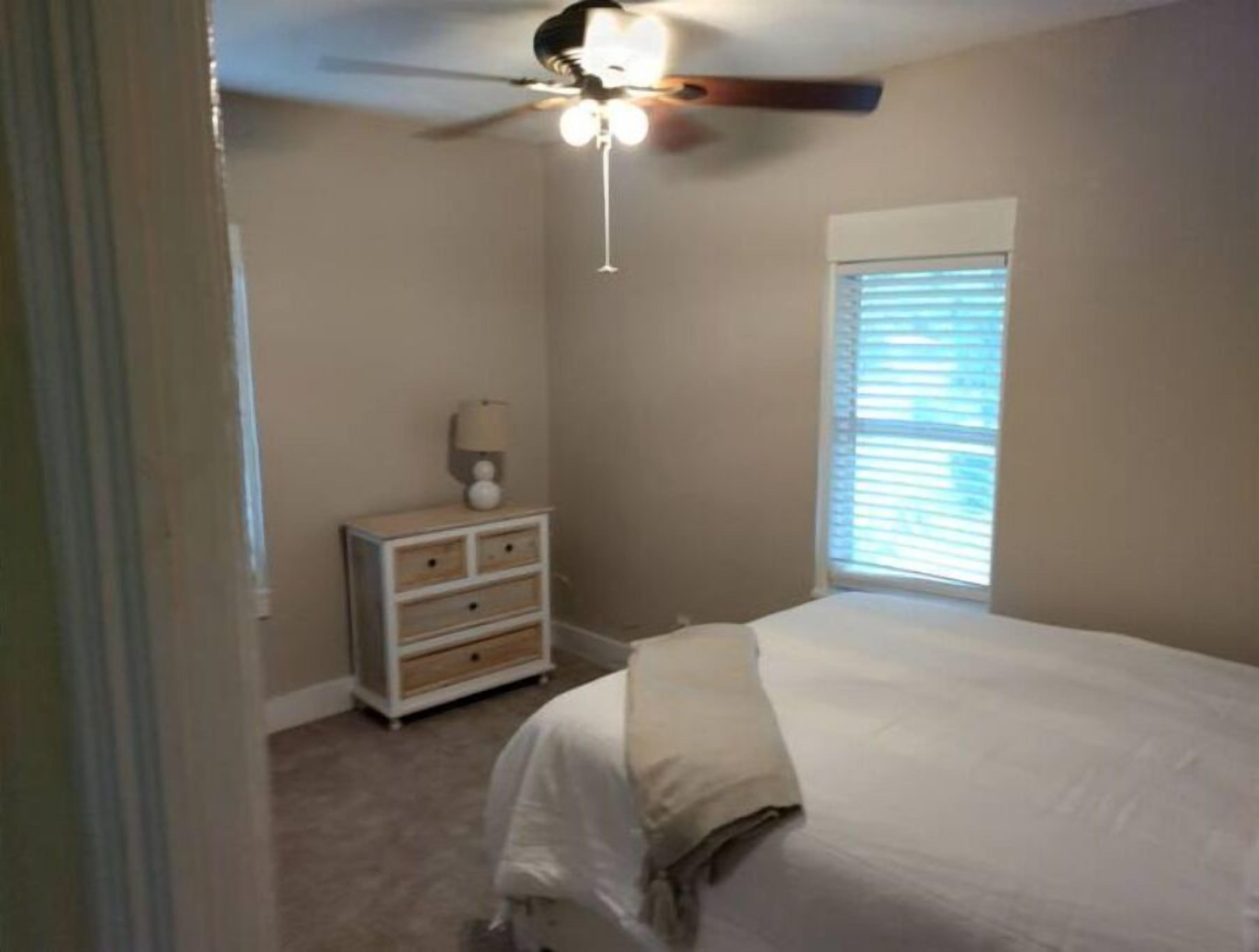 A bedroom with a bed, a nightstand, a ceiling fan, and a window with blinds.