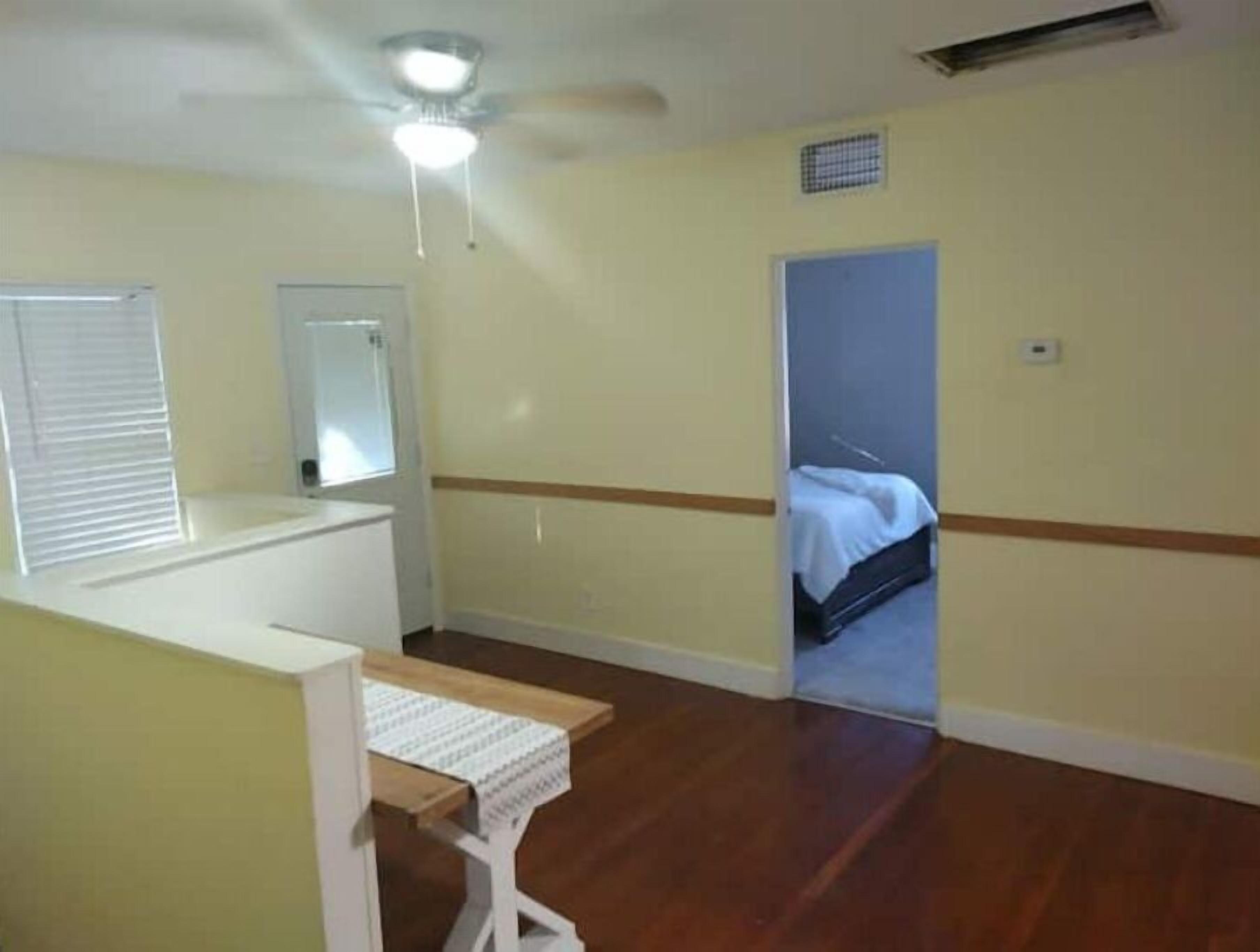 Ein kleines Hotelzimmer für eine Person mit Holzboden, einem Bett, einem kleinen Tisch und einem Fenster mit Jalousien.