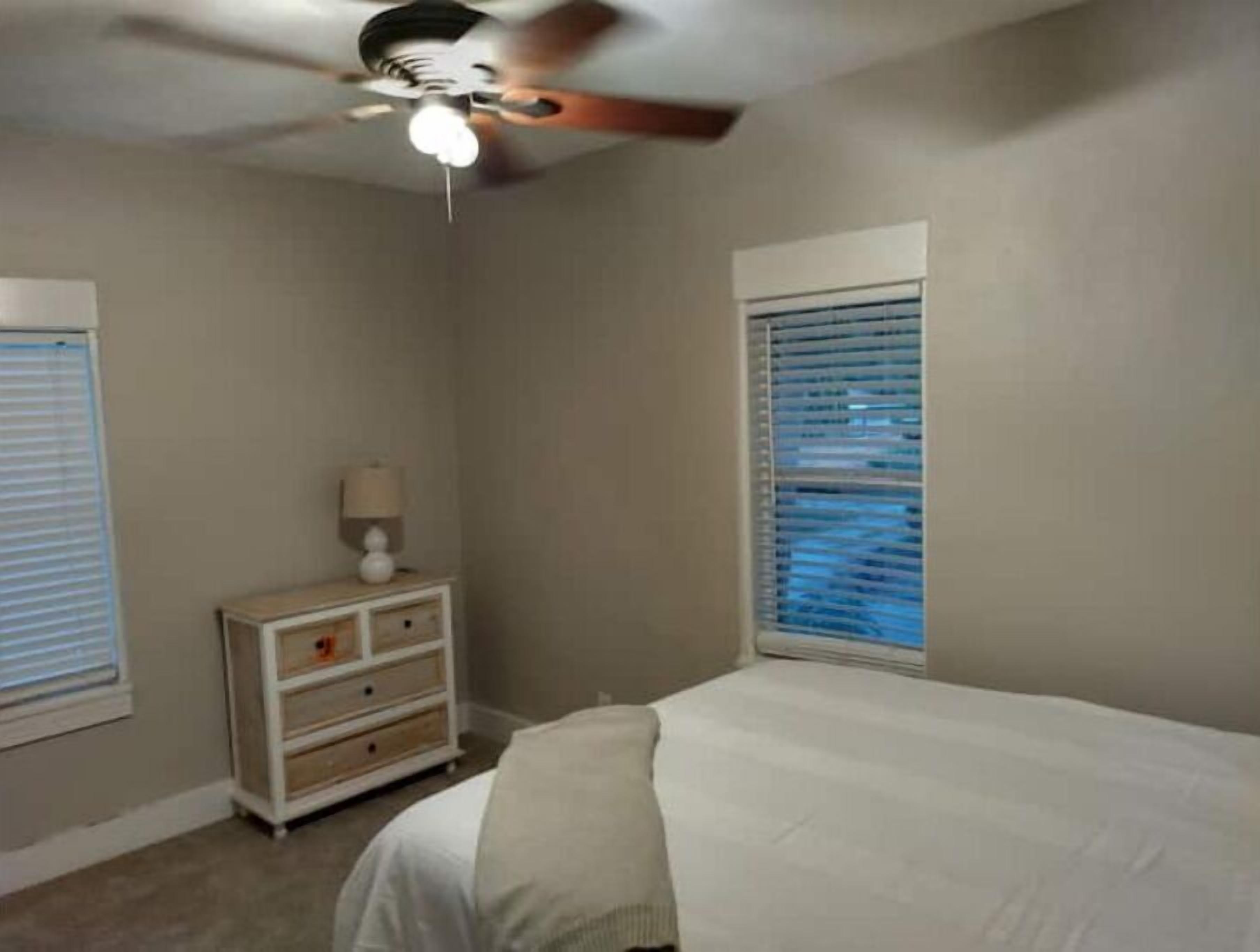 A bedroom with a bed, a nightstand, a lamp, and a ceiling fan.