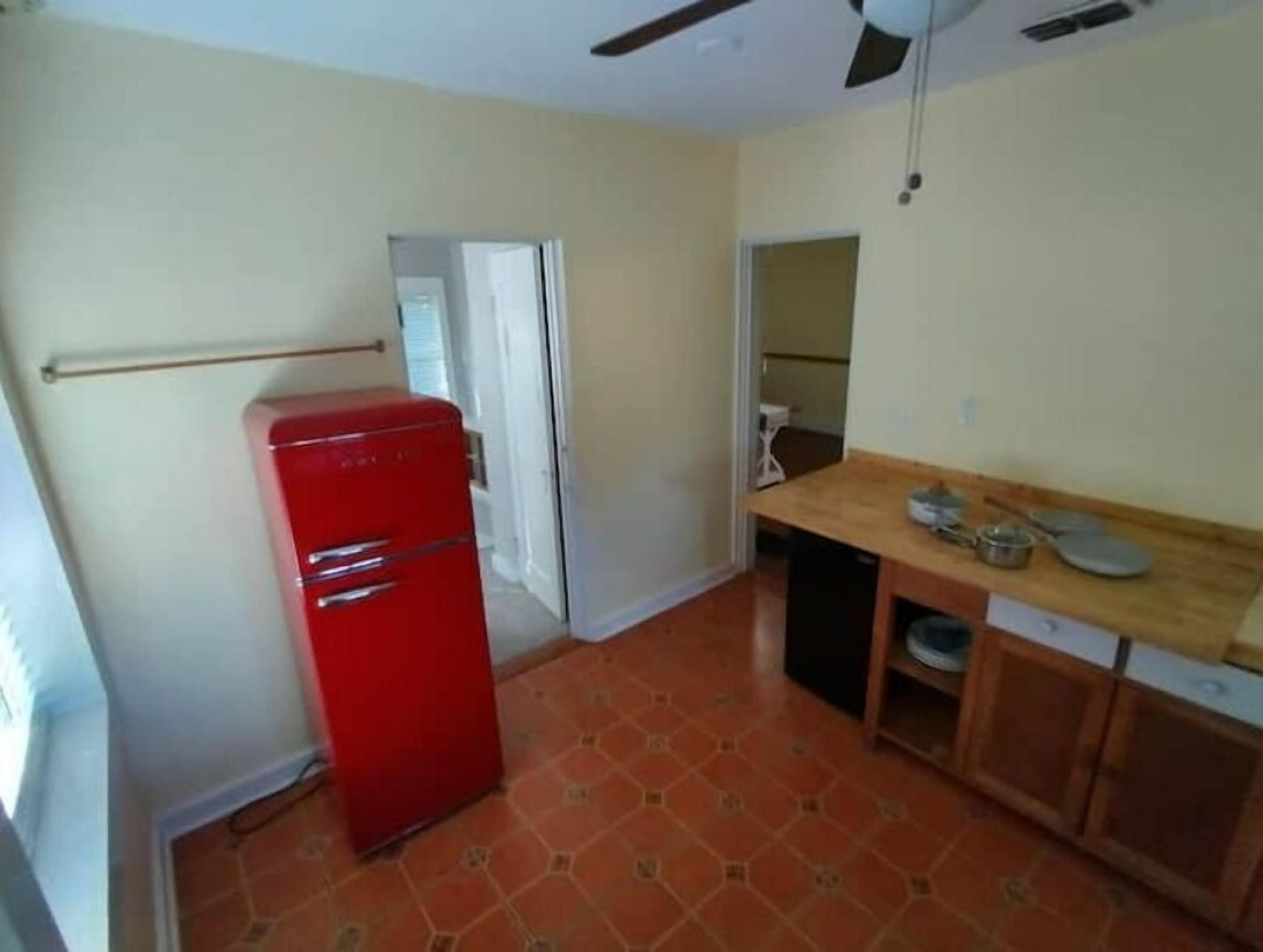 A compact kitchen with a red refrigerator, a wooden countertop, and a ceiling fan.