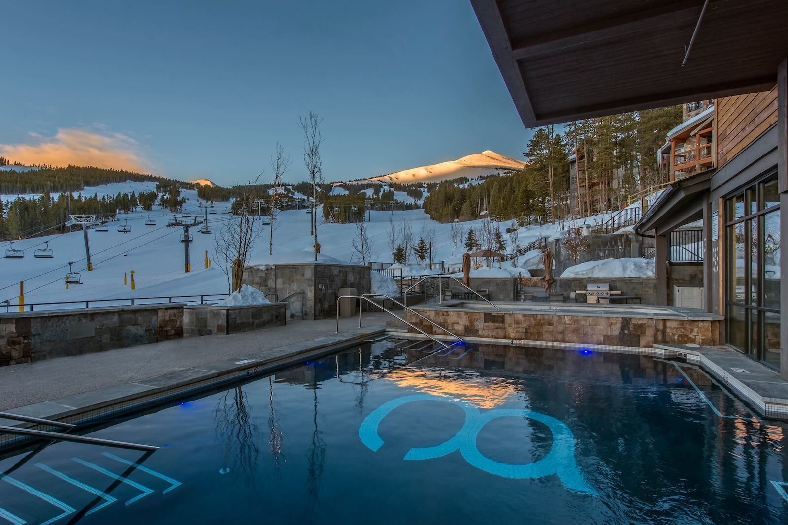 A pool area with a view of a snowy mountain and ski lift in the background.
