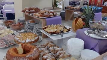 Un tavolo del buffet con diversi cibi, tra cui pasticcini, frutta e una torta.