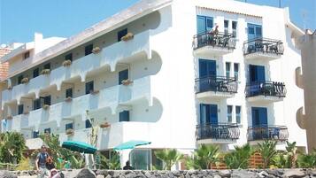Un hotel a più piani con balconi, un muro in pietra e una bandiera.