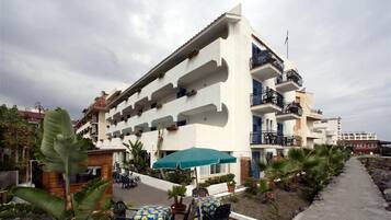 Un hotel a più piani con balconi, arredi esterni e piante tropicali.
