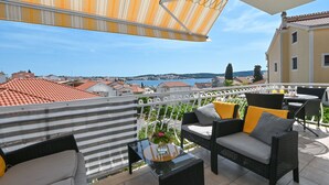 A balcony with wicker furniture, a glass table, and a striped awning.