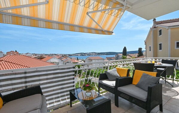 A balcony with wicker furniture, a glass table, and a striped awning.