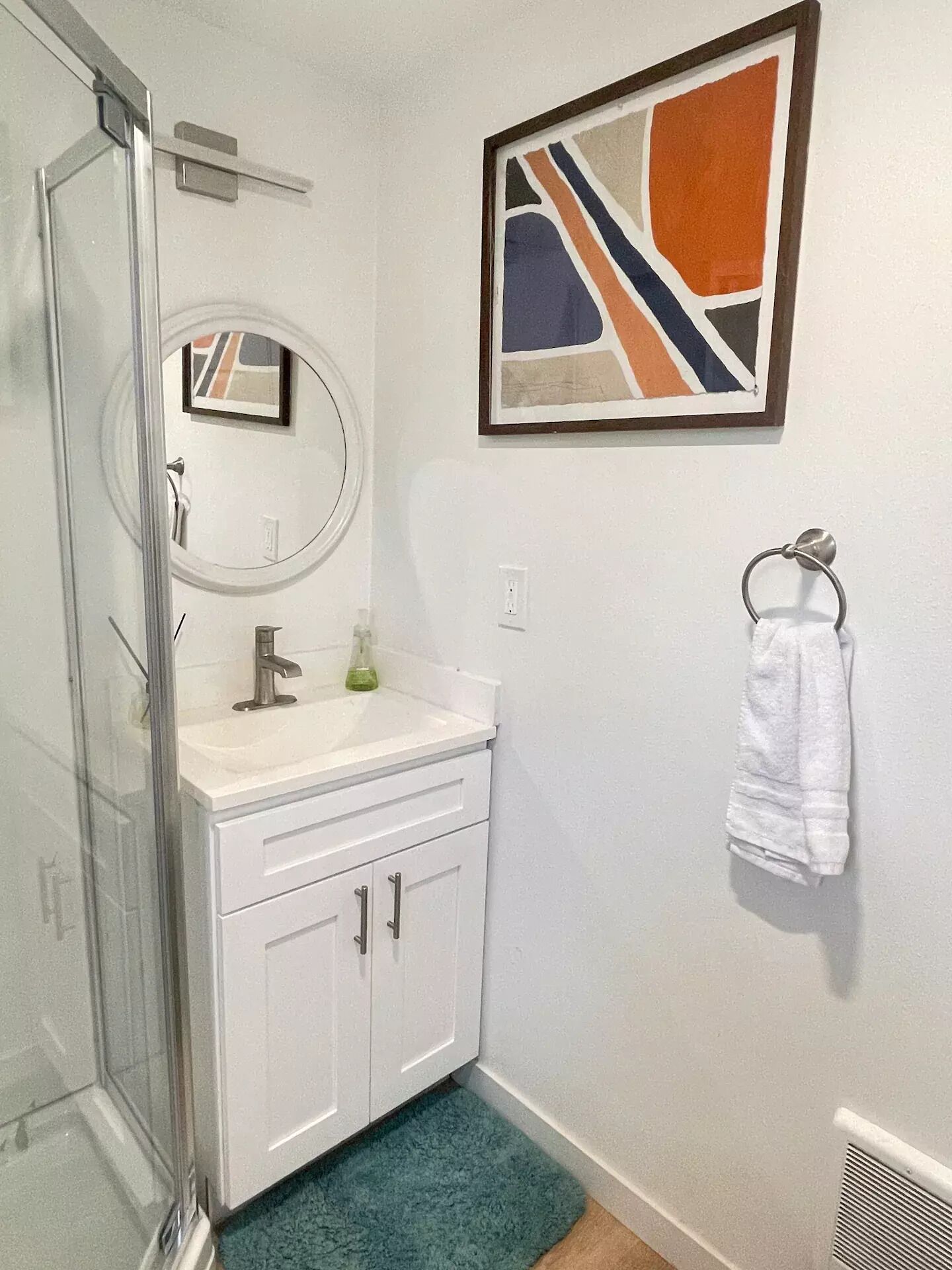 A bathroom with a glass shower enclosure, a white sink with a mirror, and a towel ring on the wall.