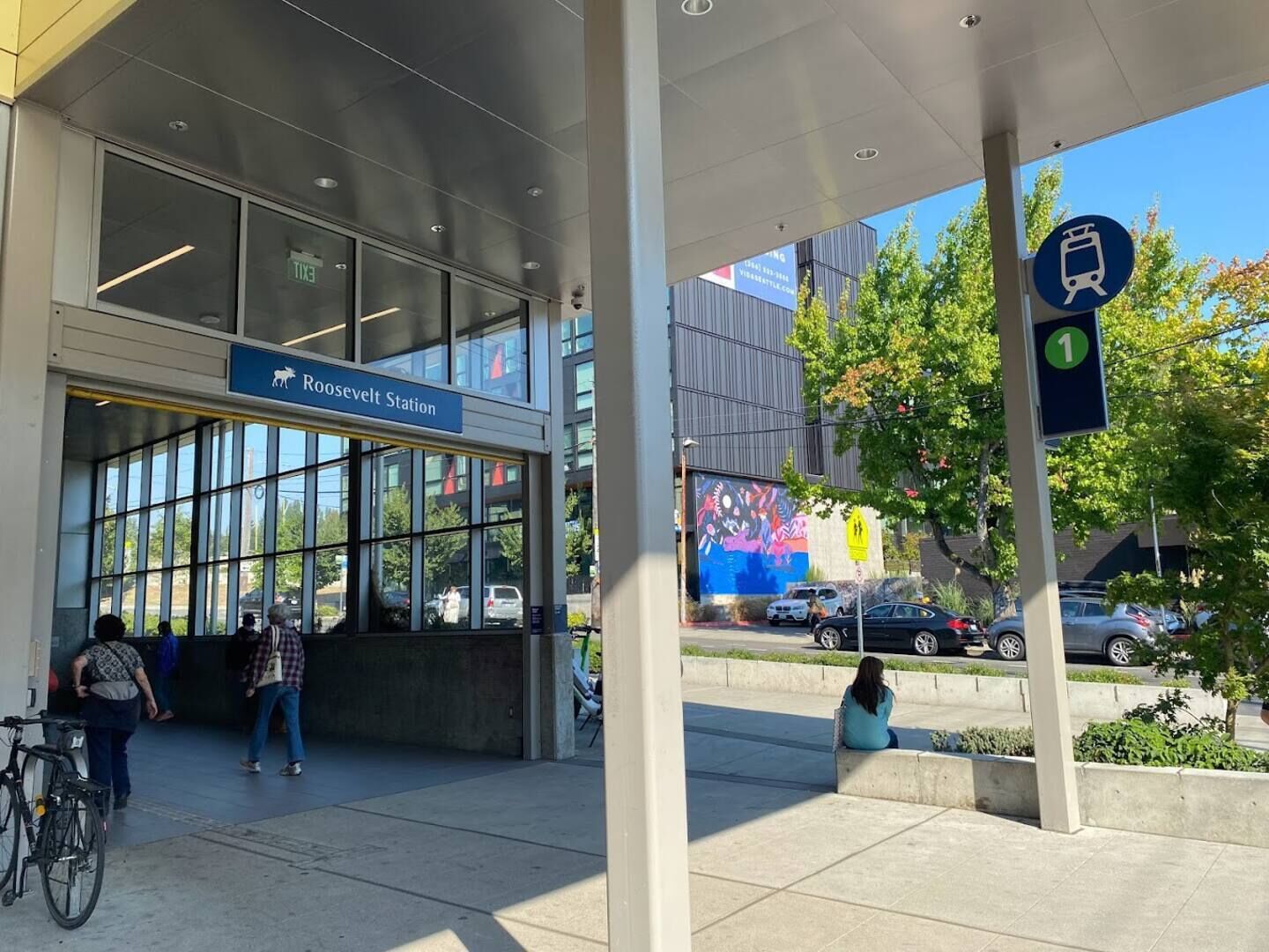En modern byggnad med en glasfasad, en skylt som visar var Roosevelt Station ligger och en skylt för en spårvagnshållplats.