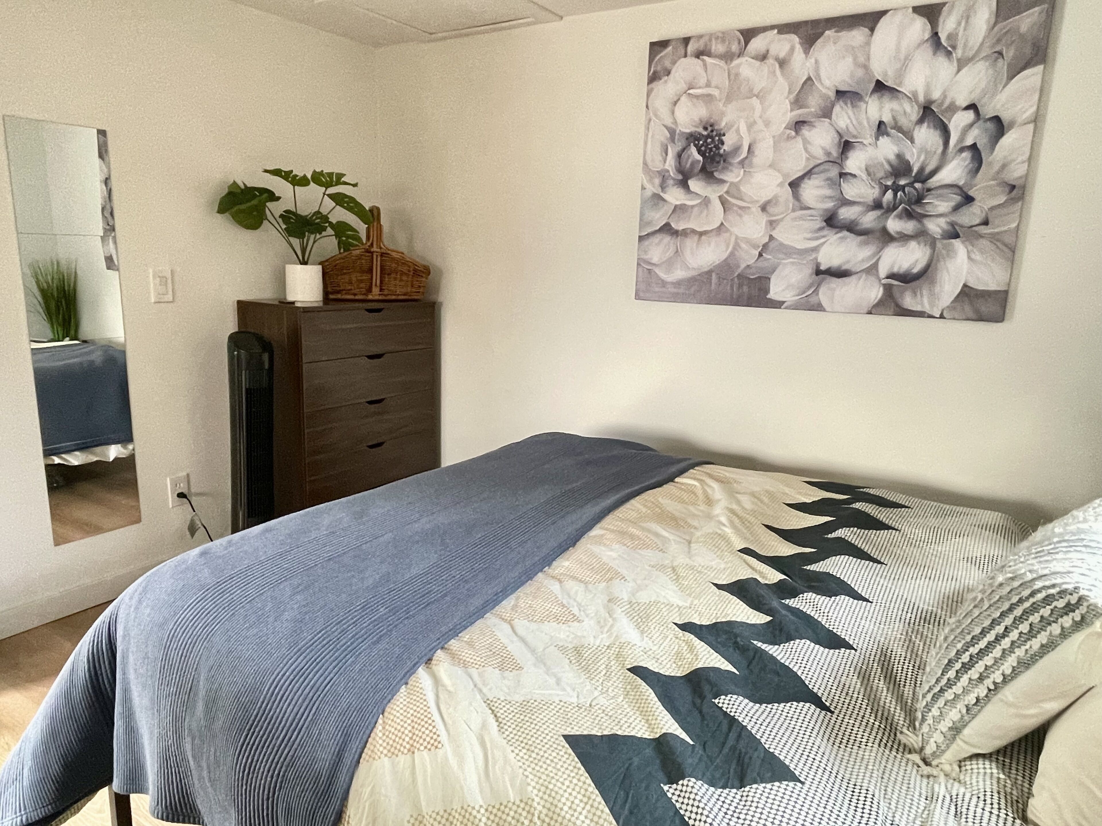 Een slaapkamer met een bed, een dressoir, een spiegel en een bloemschilderij aan de muur.