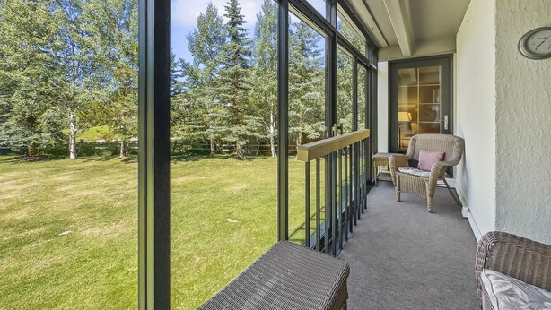 Ein Balkon mit Blick auf einen Rasen und Bäume, ausgestattet mit Korbmöbeln und einer Bank.
