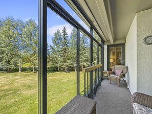 A balcony with a view of a grassy yard and trees, furnished with wicker chairs and a bench. - Ski in, walk out, East Village Condo on the golf course. WH102 (Copper Mountain)