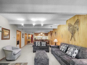 A living room with grey sofas, a grey armchair, and a wooden wall with a butterfly decoration.