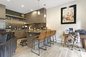 A modern kitchen with a bar area, wooden cabinets, and a dining area with a bar stool and a chair.