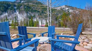 A patio with blue Adirondack chairs and a small round table, overlooking a mountainous landscape with a red-roofed building in the distance. - Cozy Vail Retreat, On Shuttle Route, BBQ (Vail)