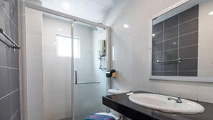 Une salle de bain moderne avec une douche à l’italienne en verre, des toilettes blanches et un plan de toilette noir avec un lavabo blanc.