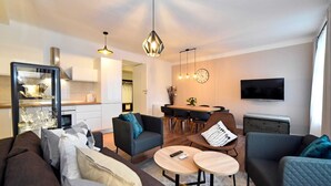A modern living room with a sofa, two armchairs, a coffee table, and a dining area with a TV and clock. - Moin - Moin Apartment and Suite Zagreb (Zagreb)
