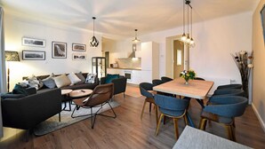 A modern living room with a sofa, chairs, and a dining table. There is a kitchen in the background. - Moin - Moin Apartment and Suite Zagreb (Zagreb)